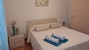 A neatly made bed with two rolled towels, a bedside table with a lamp, and a wall-mounted artwork. - Agriturismo La Tortorella (Grosseto)