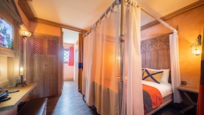 Quarto com cama de dossel, piso de madeira e escrivaninha com um banco.