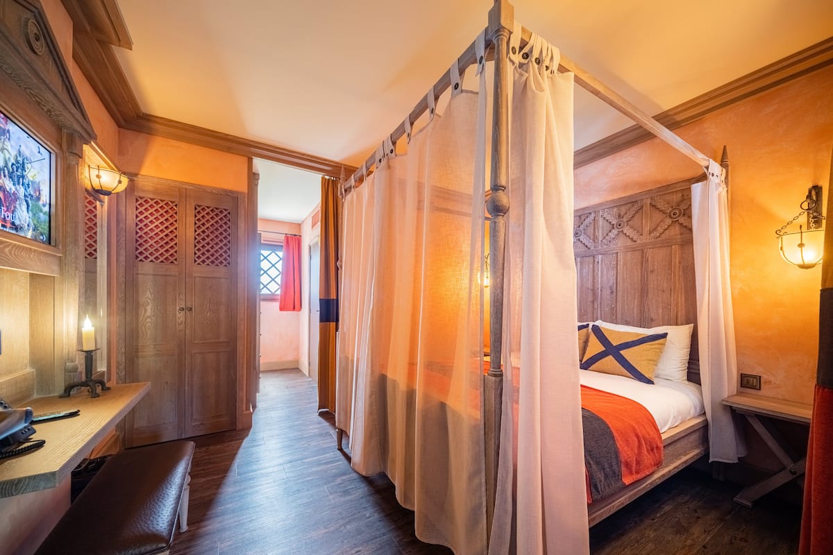 Un dormitorio con cama con dosel, suelo de madera y un escritorio con una banca.
