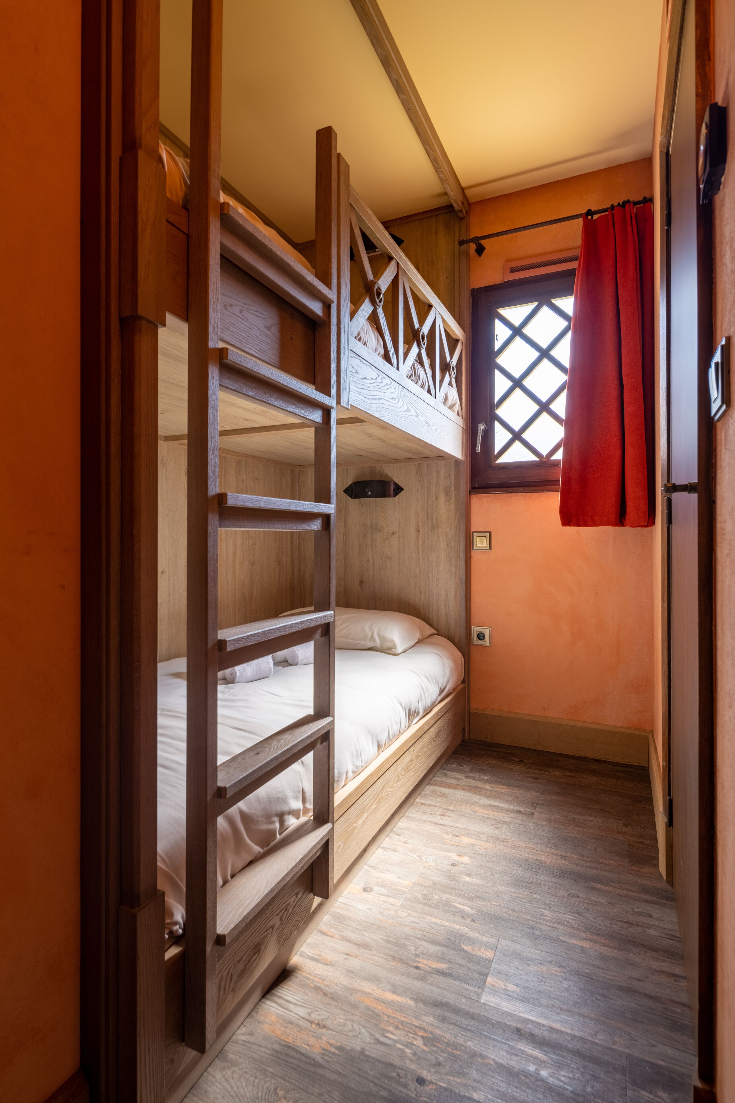 Habitación con literas, paredes de madera y una ventana con cortinas rojas.