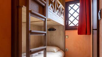 Habitación con literas, paredes de madera y una ventana con cortinas rojas.