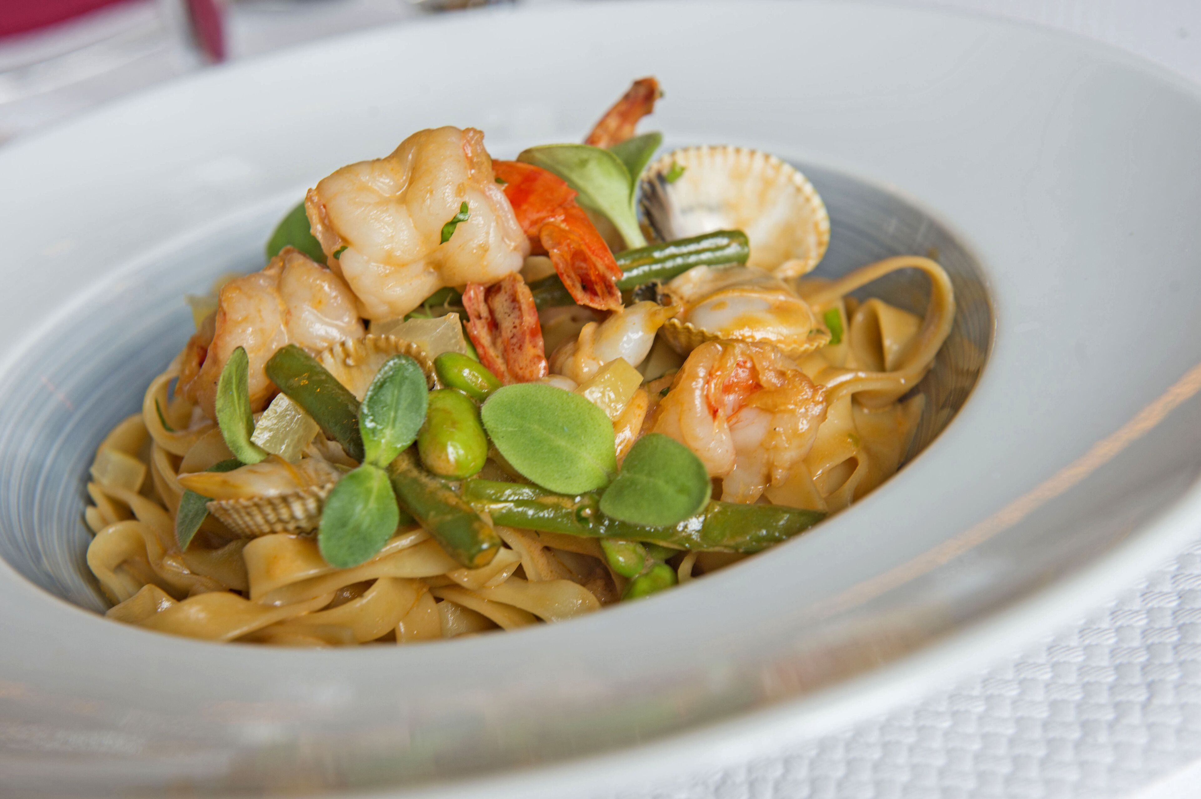 A plate of pasta with shrimp, clams, and green vegetables.