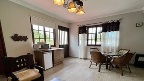 A room with a wooden dining table, chairs, a small kitchenette, a sofa, and a wooden bench.