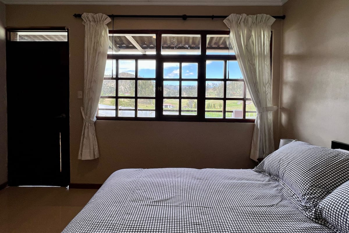 A bedroom with a large window, a bed with a checkered bedspread, and a door.
