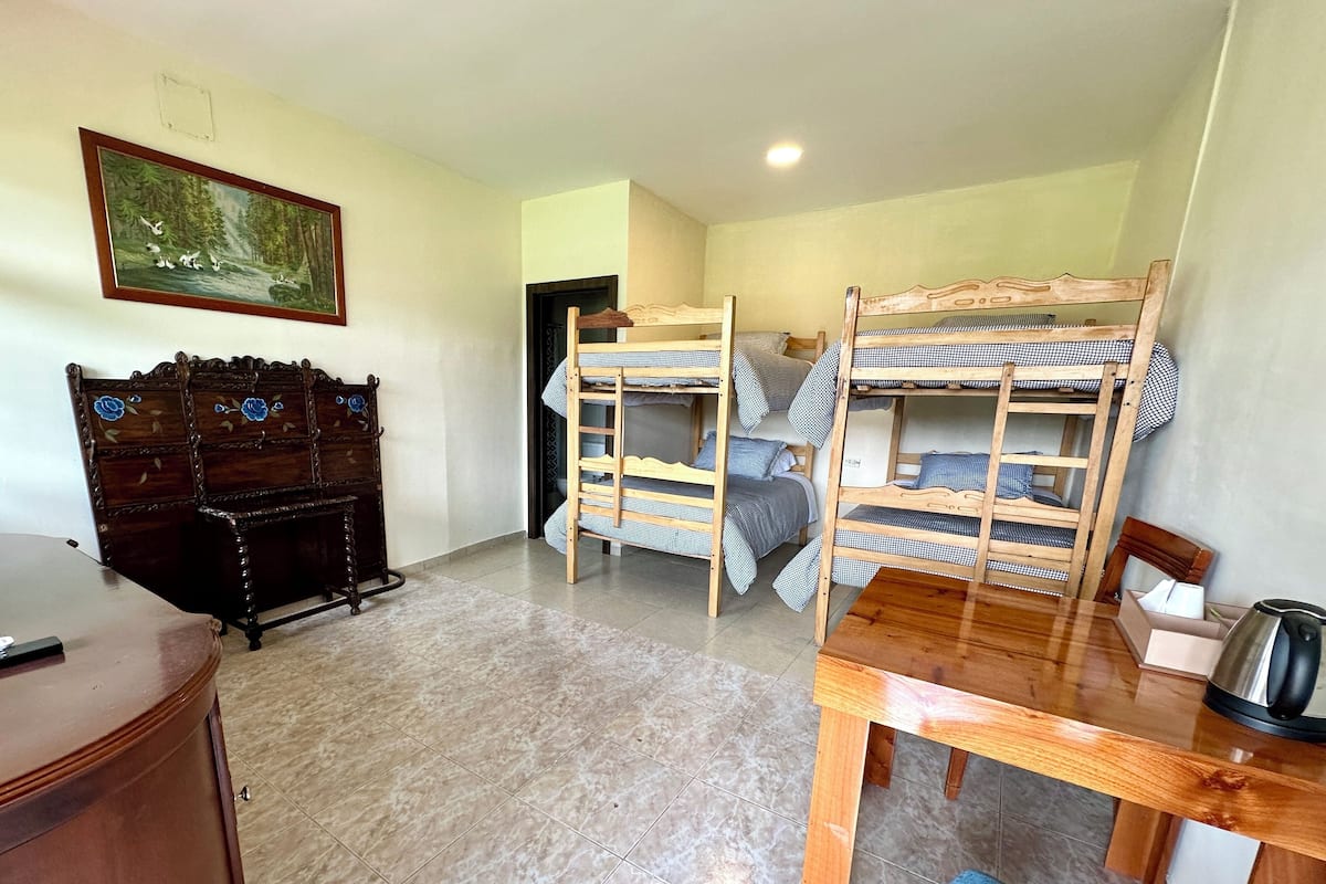 A dormitory room with bunk beds, a wooden desk, a dresser, and a painting on the wall.