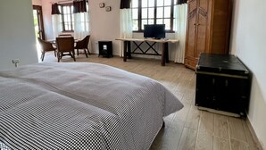 A room with a bed, a desk with a computer, a wardrobe, and a dining area with chairs and a table.