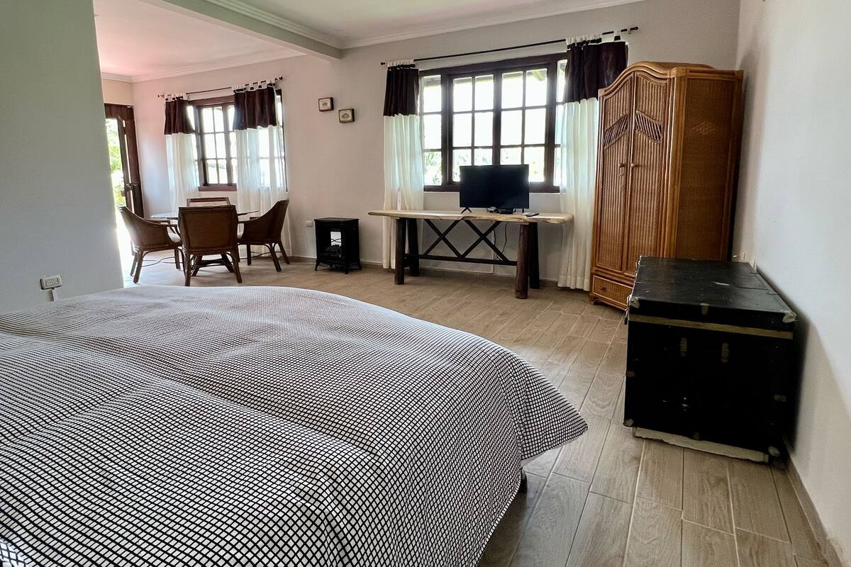 A room with a bed, a desk with a computer, a wardrobe, and a dining area with chairs and a table.