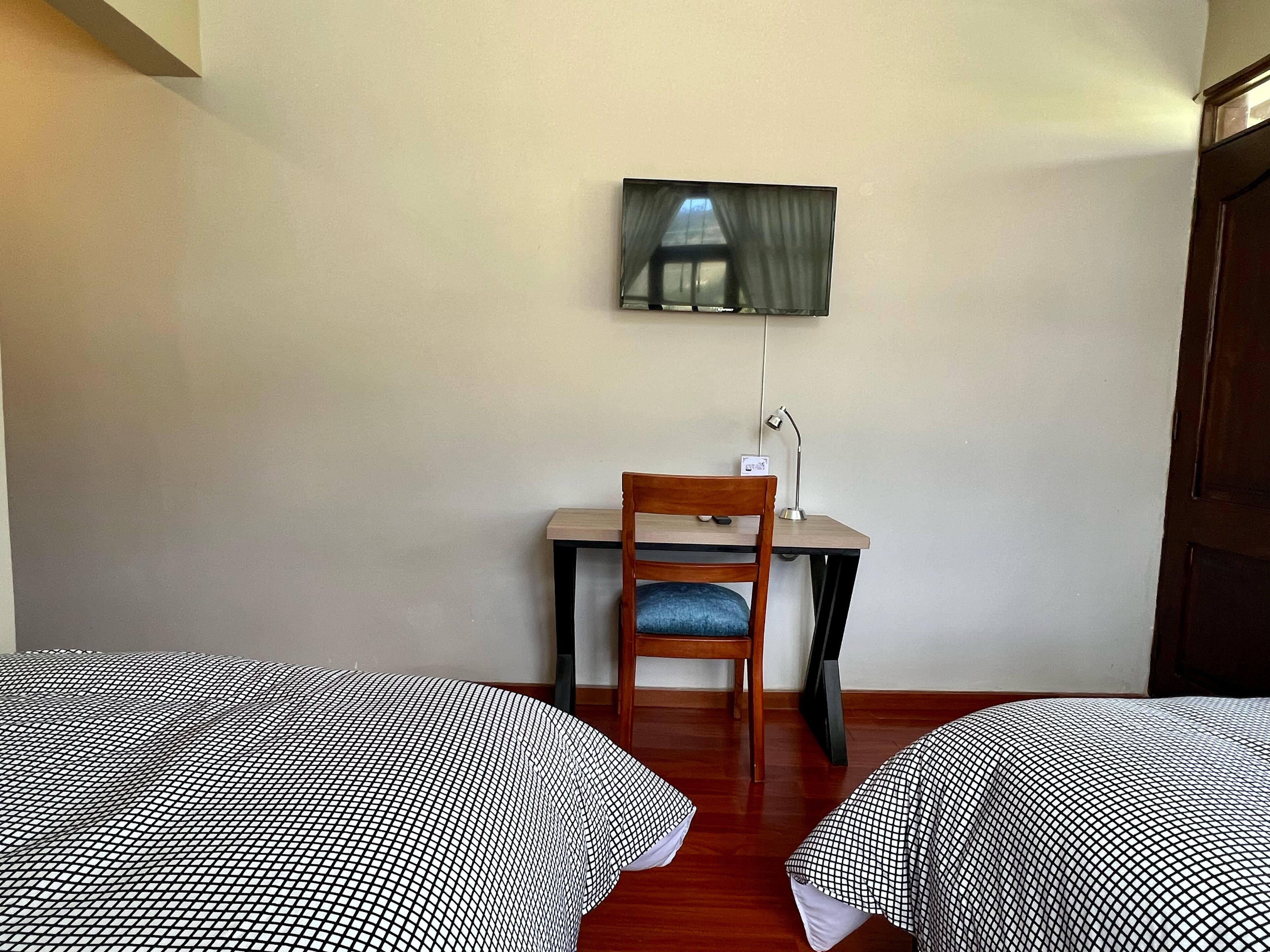 Una habitación con dos camas, un escritorio, una silla y un televisor fijado a la pared.