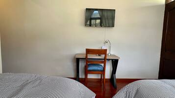 Una habitación con dos camas, un escritorio, una silla y un televisor fijado a la pared.