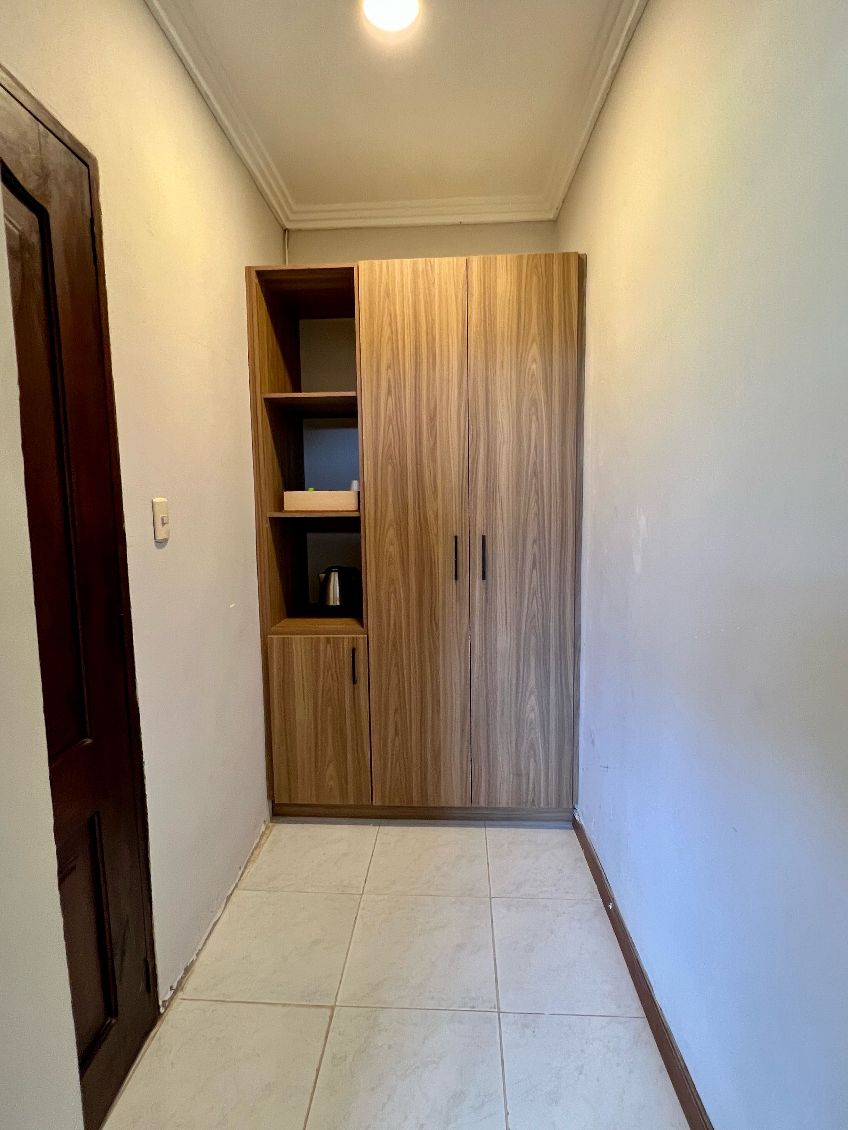 Un pasillo con un armario de madera, suelo de baldosas y una puerta a la izquierda.