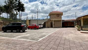 Un estacionamiento con suelo de baldosas estampadas, un edificio de techo en teja roja y algunos coches aparcados.