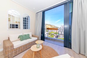 Uma sala de estar moderna com um sofá de vime, uma mesa redonda pequena e uma grande janela com vista para a cidade.