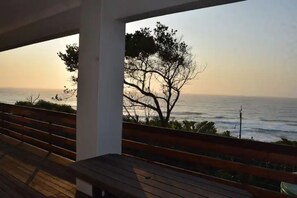 A wooden bench overlooking a coastal view with a tree and ocean. - The Beach House (Umkomaas)