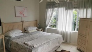 Et soveværelse med seng, natbord, skab, loftventilator og et vindue med gardiner.