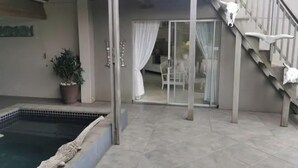 Et overdækket udendørs område med en pool, en trappe og en skydedør, der fører til en terrasse.