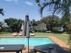 A swimming pool with lounge chairs and umbrellas, surrounded by lush greenery.