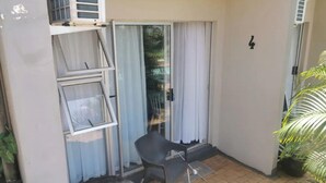 En lille balkon med en stol, skydedør og en potteplante.
