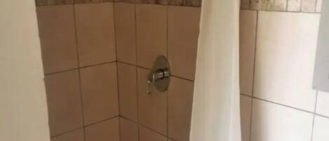 A small, tiled shower area with a white curtain, a visible showerhead, and a sink with a blue basin.
