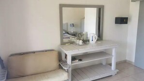 Une petite pièce propre, avec un canapé, une console blanche agrémentée d’un miroir et une bouilloire.