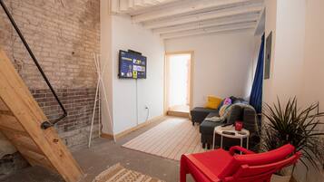 Een kamer met een bakstenen muur, een houten trap, een flatscreen televisie, een bank, een rode stoel en een potplant.