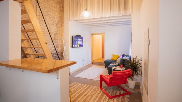 A modern living space with a wooden loft, a red chair, a potted plant, and a television on the wall.