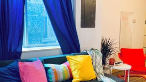 A modern living room with a blue sofa, colorful cushions, a small white table, and a red chair.