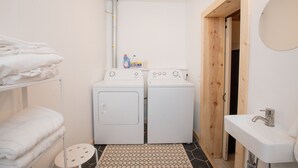 A compact laundry room with two washing machines, a small sink, and a towel rack.