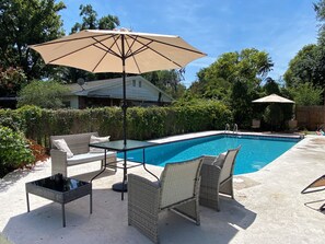 A backyard with a swimming pool, outdoor furniture, and a large umbrella.