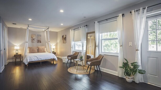 Ein Schlafzimmer mit Himmelbett, zwei Nachttischen, einem Sessel, einem runden Teppich und einem Blumentopf.