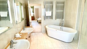 Un baño moderno con dos lavamanos, una bañera grande y una cabina de ducha con paredes de vidrio.