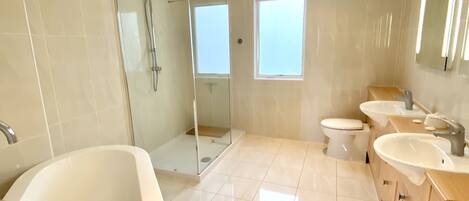 A modern bathroom with a large bathtub, a glass-enclosed shower, and two sinks.