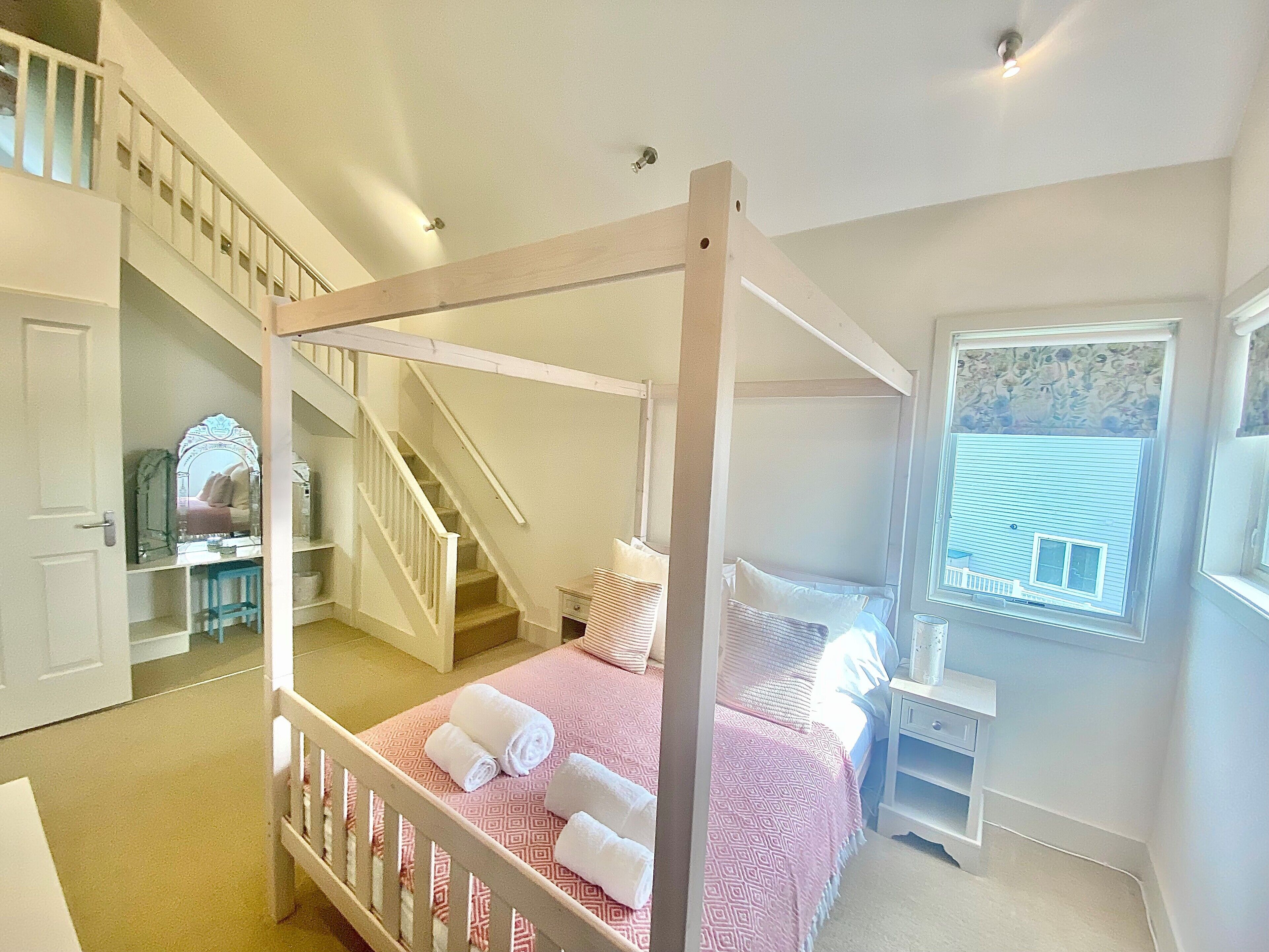 A four-poster bed with rolled towels, a staircase, a window with a view, and a mirror.