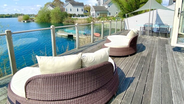 Una terraza de madera con mobiliario de mimbre y vista a un lago.