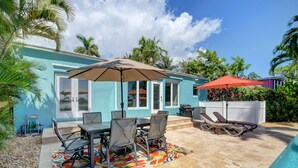 A poolside area with a dining table, chairs, and a colorful rug.