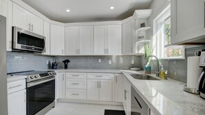 A modern kitchen with white cabinets, stainless steel appliances, and a large window providing natural light.
