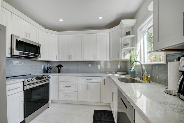 A modern kitchen with white cabinets, stainless steel appliances, and a large window providing natural light.