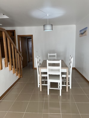Un comedor con una mesa y sillas de madera, un ventilador de techo y una escalera.