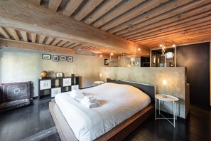 A modern bedroom with a wooden ceiling, a large bed, bedside tables, a bench, and wall-mounted artwork.