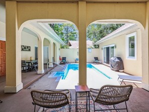 A pool area with two wicker chairs, a table, and a covered grill. - Beautiful Home w/ Pool & Game Room (Hilton Head Island)