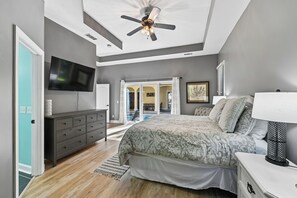 A bedroom with a bed, dresser, TV, ceiling fan, and a view of an outdoor area. - Beautiful Home w/ Pool & Game Room (Hilton Head Island)