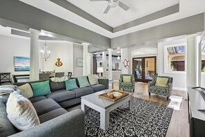 A modern living room with a grey sectional sofa, a white coffee table, patterned rug, and a ceiling fan. - Beautiful Home w/ Pool & Game Room (Hilton Head Island)
