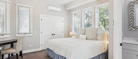 A bedroom with a bed, a desk, a chair, a ceiling fan, and large windows.