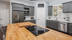 Een moderne keuken met grijze kastjes, roestvrijstalen apparatuur en een houten kookeiland met een zwart inductiefornuis.