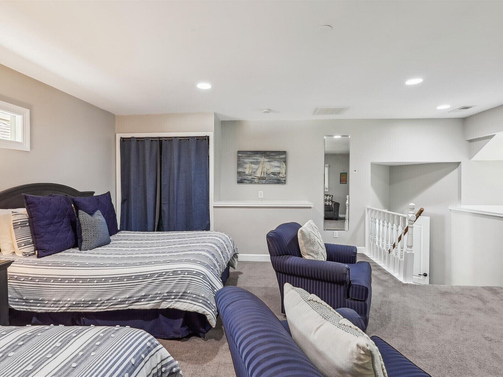 A bedroom with two beds, a chair, a bench, and a staircase.