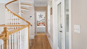 A hallway with a wooden staircase, a bed with floral bedding, and a door with frosted glass panels.