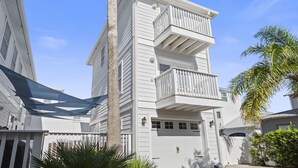 A multi-story residential building with a white exterior, a balcony on the upper floor, and a garage door.