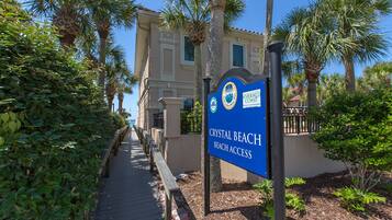 Señal para el acceso a la playa Crystal Beach, con un camino que lleva a un edificio rodeado de palmeras.