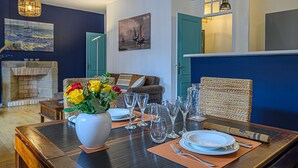 Un coin repas avec une table dressée pour quatre personnes, un vase de fleurs et une cheminée en arrière-plan.
