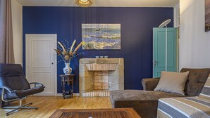 Un salon avec une cheminée en pierre, un mur bleu, un fauteuil en cuir marron, un canapé marron et une table basse en bois.