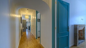 Un couloir doté d’un plancher en bois, de portes de couleur turquoise et d’une cheminée en pierre.